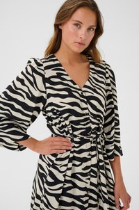 Robe imprimée zèbre avec une palette de couleurs noir et crème, dotée d'un col en V, de détails en boutons et d'une taille cintrée. Fabriquée dans un tissu lisse.