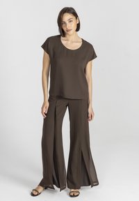 Brązowa bluzka z okrągłym dekoltem, krótkimi rękawami, w połączeniu z wysokim stanem, szerokimi spodniami z bocznymi rozporkami i gładką fakturą materiału.