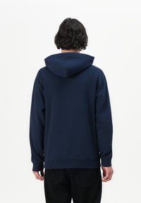 Sweatshirt azul-marinho com capuz ajustável, mangas compridas e punhos canelados. Textura suave com um corte relaxado e sem padrões proeminentes.