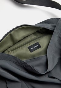 Grå nylon taske med grøn inderside, der har en lynlåslomme og et synligt sort mærke, PULL&BEAR, indeni.