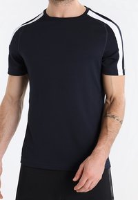 Marineblaues Sport-T-Shirt aus leichtem, strukturiertem Stoff. Mit weißen Akzenten an den Schultern und Rundhalsausschnitt. Kurze Ärmel.