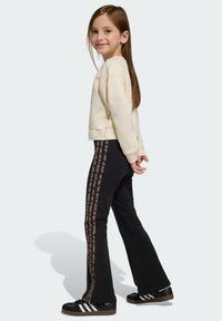 Felpa cremosa, pantaloni neri a zampa con righe marroni a stampa animalier e sneakers nere con strisce bianche. Capelli lunghi parzialmente coprono le spalle.