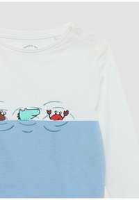 Witte langoeve shirt met blauwe onderkant. Bevat een speelse grafiek van een krokodil, krab en zeewier boven de waterlijn. Drukknoopjes op de schouder.