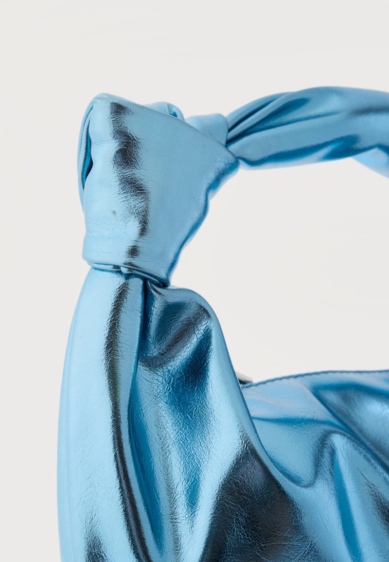 Bolso de mano azul metálico brillante con detalle de asa anudada, textura suave y superficie ligeramente reflectante.