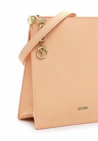 Lyserød tekstureret lædertaske med en tynd skulderrem, guldfarvet logohængsmykke og lille guldfarvet mærke med brandnavn foran.