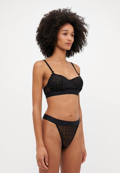 Zwart lingeriesetje met een doorzichtige, gestippelde bralette met verstelbare bandjes en bijpassende thong, beide versierd met een logo band.