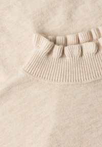 Gros plan d’un tissu tricoté beige avec un détail de bord-côte ou de col froncé.