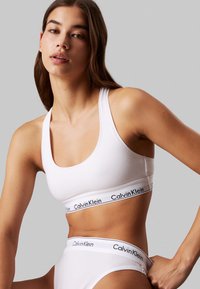 Fehér pamut sportmelltartó széles elasztikus pánttal, fekete "Calvin Klein" logóval, fehér, azonos színű bugyival párosítva. Simább textúra és minimalista dizájn.