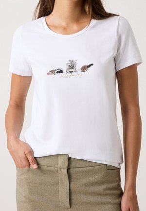 Chemise blanche à manches courtes ornée d'illustrations de rouge à lèvres, flacon de parfum et vernis à ongles au-dessus du texte « simplement glamour », portée par une femme.