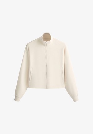 Jachetă crem cu fermoar, guler înalt, mâneci lungi, manșete elastice și două buzunare verticale în față.