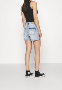 Džíny šortky v světle modré barvě s opotřebovaným vzhledem, s vysokým pasem, ohrnutým lemem a dvěma zadními kapsami. V kombinaci s černými vysokými teniskami.