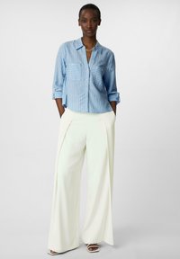 Light blue striped button-up shirt with two chest pockets, paired with wide white trousers. Smooth fabric and relaxed fit design.