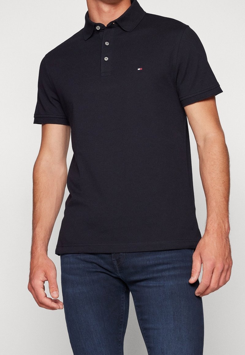 Marinblå polo med klassisk krage, tre-knappsknäppning och en liten logotyp på bröstet. Fitted design. Gjord av bomull.