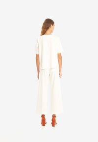 Vit tvådelad outfit bestående av en kortärmad topp och vida byxor, matchad med orange, strukturerade klackar. Rent snitt och minimalistisk design.