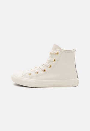 Wysokie kremowe sneakersy z białymi sznurowadłami, złotymi przelotkami, gumową podeszwą i prostym przeszyciem, pokazane z profilu na białym tle.