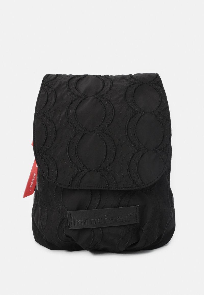 Mochila negra de nailon con un patrón de ondas acolchadas, una solapa plegable y un parche con el logotipo en la parte frontal. Incluye una etiqueta roja en contraste.