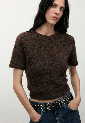 Suéter corto de manga corta de textura marrón con cuello redondo, combinado con jeans azul de cintura alta y un cinturón negro con tachuelas plateadas.