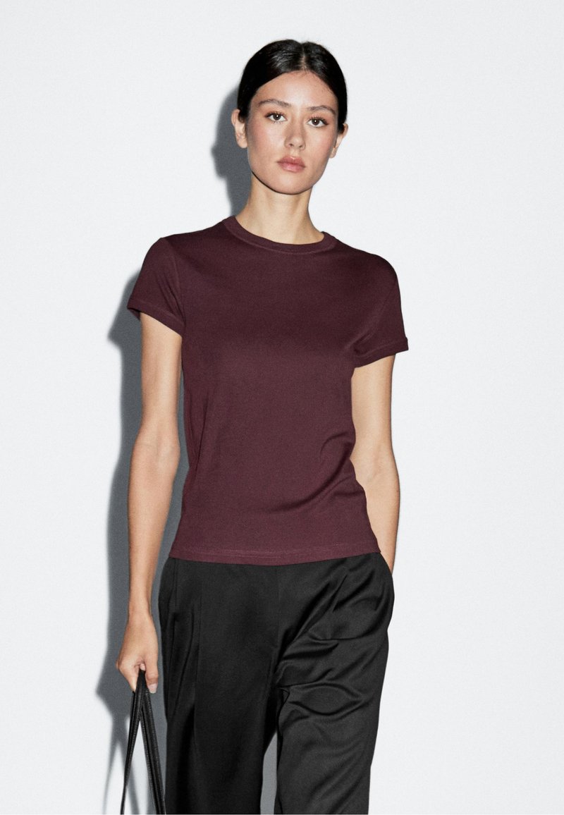 Bordeauxkleurig T-shirt met korte mouwen van zacht katoen met een ronde hals, gecombineerd met losse zwarte broek en een zwarte handtas.