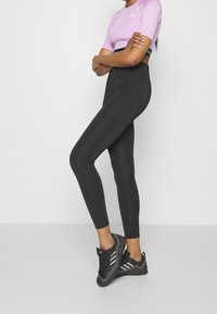 Leggings negras de cintura alta hechas de material elástico, combinados con una camiseta ajustada de manga corta en color lila y zapatillas deportivas negras.