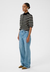 Melna un balta svītrainā adīta džemperis ar īsām piedurknēm, pogu aizdare, apvienots ar gaiši ziliem platiem biksēm un brūnām norādītām kurpēm.