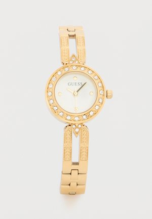 Auksinis „Guess“ rankinis laikrodis su kristalais puošta bezelės dalimi, balta ciferblatu, trimis auksinėmis rodyklėmis ir tekstūruota grandinėlės apyranke.