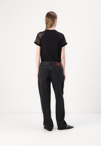 Black t-shirt with sheer short sleeves, paired with dark straight-leg jeans featuring a leather patch on the waistband and two back pockets.