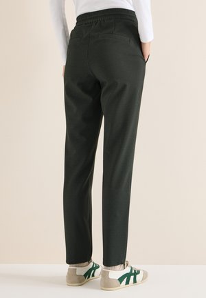 Pantaloni verde scuro con finitura strutturata, vita elastica e due tasche posteriori, abbinati a sneakers bianche e verdi.