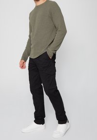 Olijfgroen geribbelde trui, ronde hals, lange mouwen. Gecombineerd met zwarte cargobroek met zijzakken en witte sneakers.