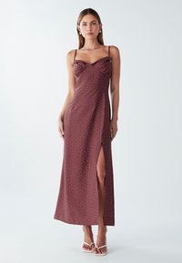 Burgundská maxi šaty s priliehavým korzetom, tenkými ramienkami a bočným rozparkom. Obsahujú textúrovanú látku s bielymi bodkami po celom povrchu.