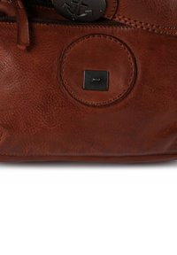 Borsa a mano in pelle marrone con una texture liscia, forma arrotondata, logo circolare e un accento metallico rettangolare sul lato.