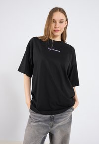Sort oversized t-shirt med korte ærmer, der har teksten "Day Dreamer" i lilla. Den er lavet af blød bomuld, har en afslappet pasform og en glat overflade.