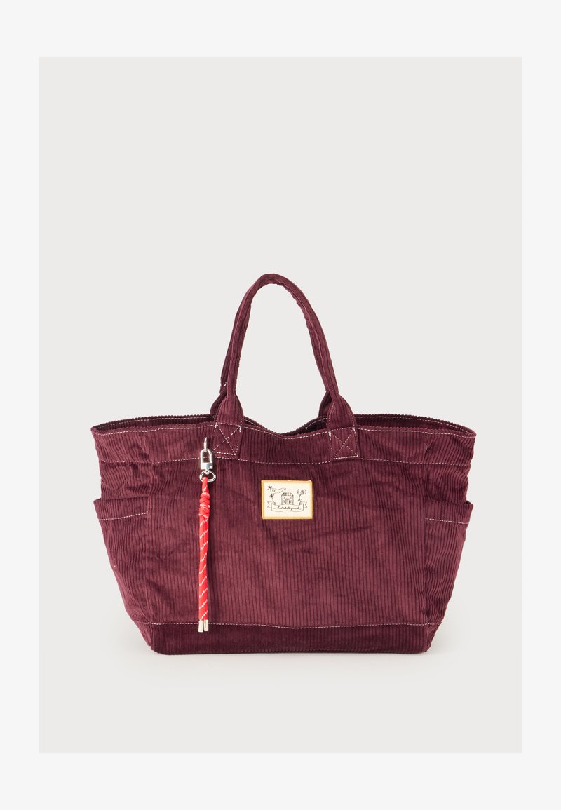 Grand sac cabas en velours côtelé bordeaux avec deux poignées, couture blanche, petite pièce à l’avant et porte-clés en corde rouge attaché à une poignée.