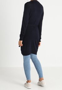 Granatowa sukienka z długim rękawem i paskiem, w połączeniu z jasnoniebieskimi rurkami i jasnymi trampkami. Gładki materiał i luźny krój.