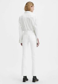 Camicia bianca con bottoni e jeans bianchi attillati. La camicia presenta un design a yoke, mentre i jeans hanno uno stile classico a cinque tasche e gamba affusolata.