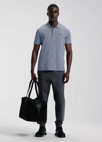Jasnoniebieska koszulka polo krótko rękawowa z kołnierzykiem i subtelnym logo, w połączeniu z węglowymi dresami i czarną torbą podróżną. Czarne buty dopełniają całość.