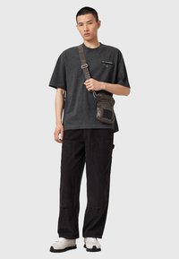 T-shirt gris surdimensionné avec logo, pantalon en velours côtelé noir et petit sac matelassé. Chaussures blanches et noires avec semelle texturée. Tissu lisse, coupe décontractée.