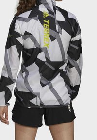 Sort-hvidt mønstret jakke med høj krave og lynlåslukning, med "Terrex"-logo i lys gul på bagsiden.