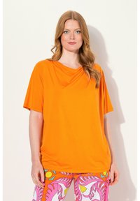Oranžový top s krátkým rukávem vyrobený z měkké, lehké látky s uvolněným střihem. Má splývavý výstřih a hladkou texturu.