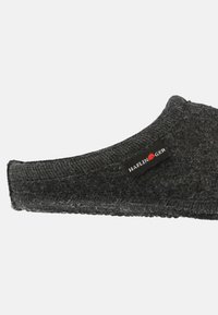 Grå uldslipper med en tekstureret overflade, lukket hæl, og et sort stofmærke med 'Haflinger' branding på siden.