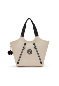 Beige tote bag with dual black zipper accents, black straps, and a round logo. Features a black pom-pom charm attached. Smooth texture.