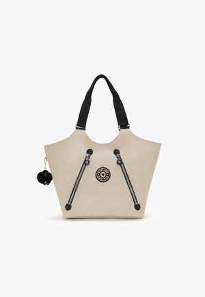 Beige tote bag with dual black zipper accents, black straps, and a round logo. Features a black pom-pom charm attached. Smooth texture.