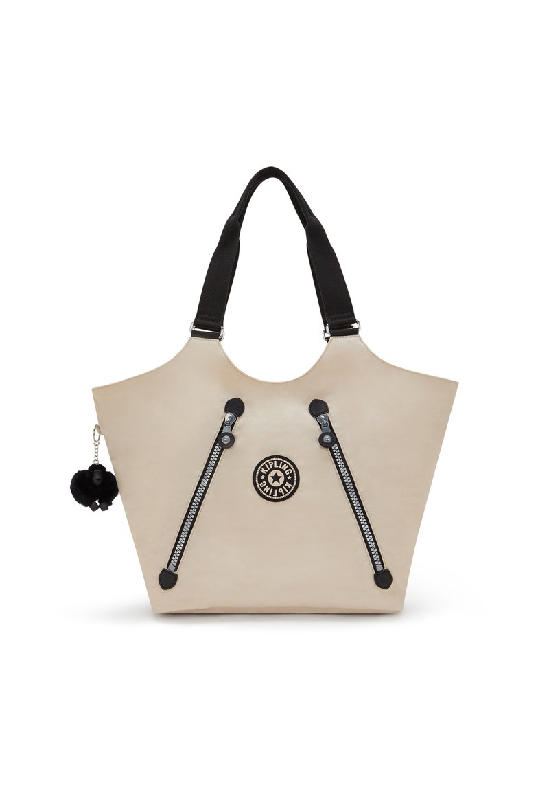 Beige tote bag with dual black zipper accents, black straps, and a round logo. Features a black pom-pom charm attached. Smooth texture.