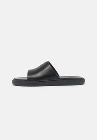 Crne klizne sandale s glatkom kožnom gornjom doradom, otvorenim prstima i ravnim gumenenim đonom. Minimalistički dizajn s elegantnom siluetom.