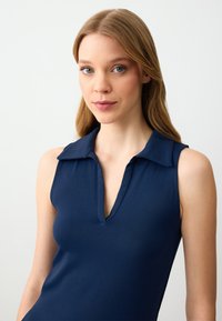 Top senza maniche color blu navy in stile polo, con colletto a punta e scollatura a V profonda. Tessuto liscio e stretchy senza schemi visibili o accenti.