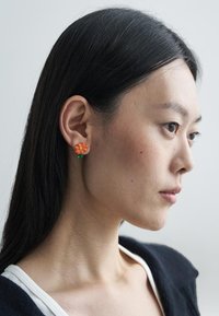 Náušnice ve tvaru oranžové květiny se zelenými akcenty, vyrobené z plastu. Design se vyznačuje podrobnými okvětními lístky a jednoduchým klipsovým záznamem.