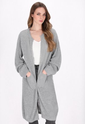 Lichtgrijze, lange gebreide cardigan met een gestructureerd oppervlak, open voorkant, twee voorkantzakken en losse mouwen. Draagt het over een wit top.