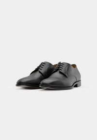 Black leather dress shoes with a smooth texture, rounded toe, and flat laces. Features a low heel and minimalistic design.