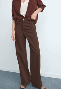 Pantalons larges marron en tissu mélangé coton avec une taille haute, des poches avant et une fermeture à bouton, associés à un haut léger.