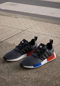 Black and gray athletic shoes with a suede finish, red and blue accents on the sole, and three black stripes on the side.