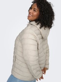 Beige puffer jacket made of quilted fabric with a hood, featuring a zipper pocket on the side and a textured, padded design.